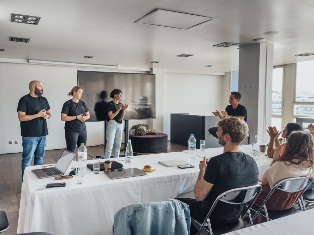 a-group-of-people-standing-around-a-table-15141200 Team members presenting in a modern office with colleagues applauding.