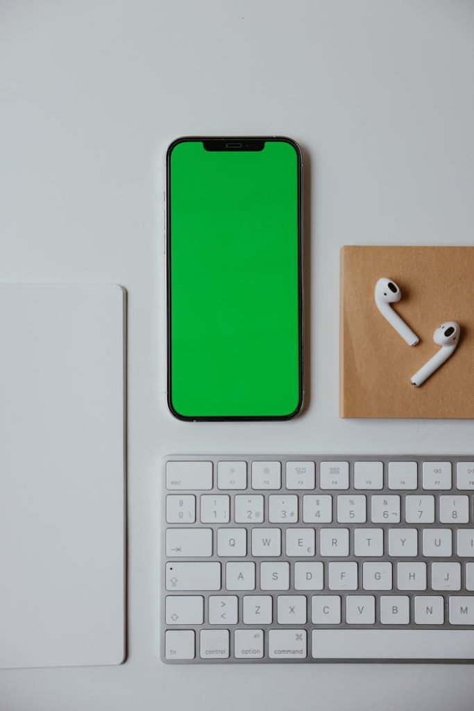 close-up-shot-of-a-cellphone-on-white-surface-7657746 Flat lay of a modern office desk with smartphone, wireless earbuds, keyboard, and card on a white surface.
